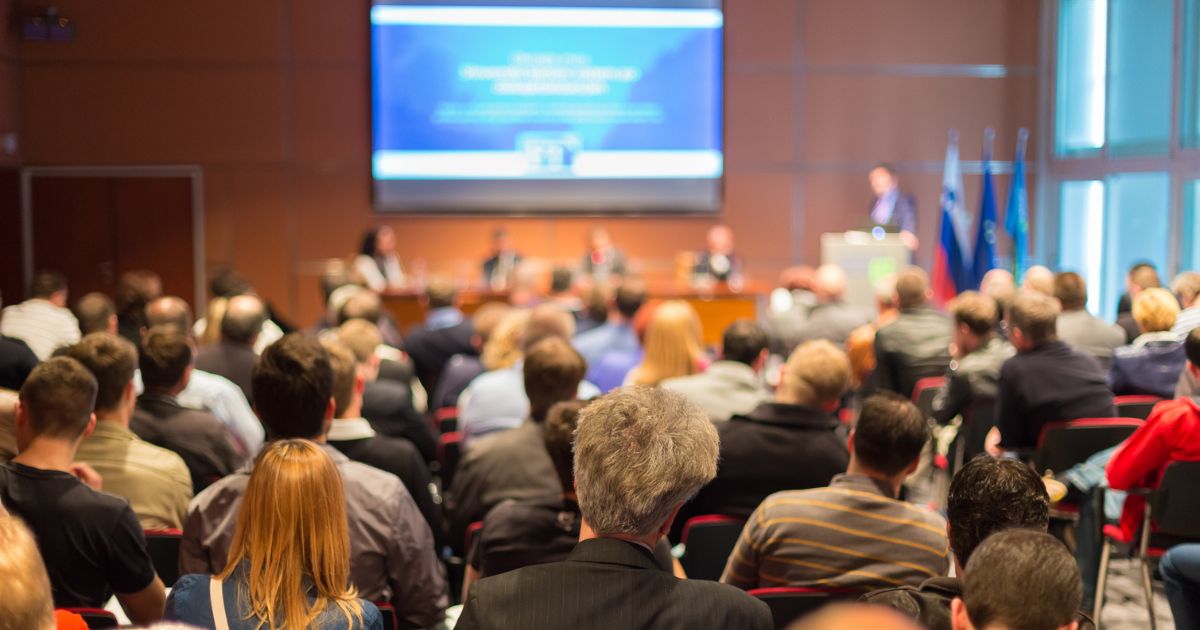 image of a conference audience and speaker to show Why Your Closing Question Fails Moving from Hero Performers to Scalable Systems